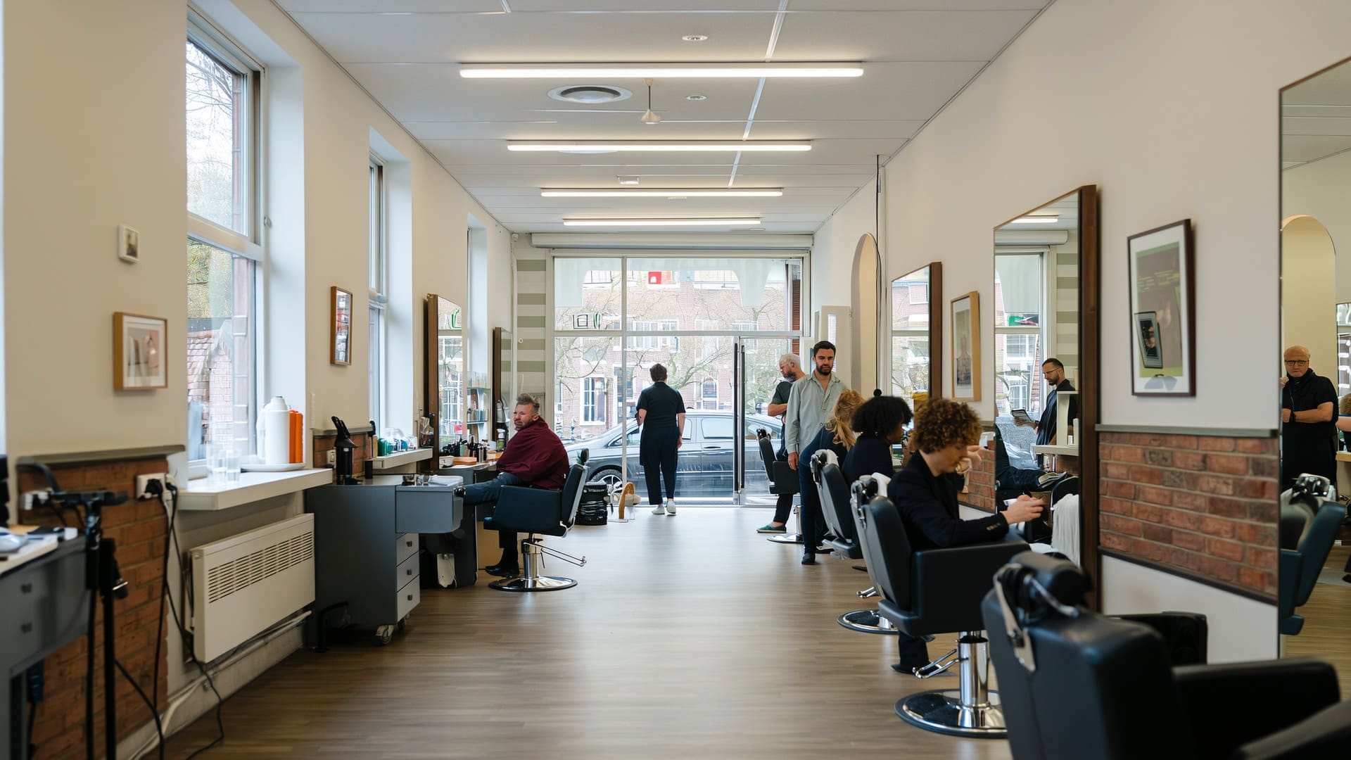 Langgerekte lichte kapsalon met stoelen en spiegels aan weerszijden en zicht op de straat